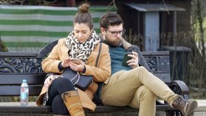 Momak i devojka sede na klupi, svako gleda u svoj telefon