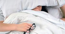 Žena spava u krevetu držeći naočare